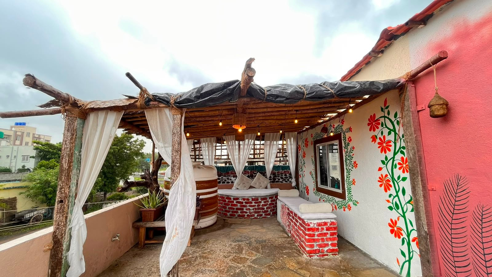 Open-air rooftop studio veranda with white drapes, rustic timber and hand-painted floral walls