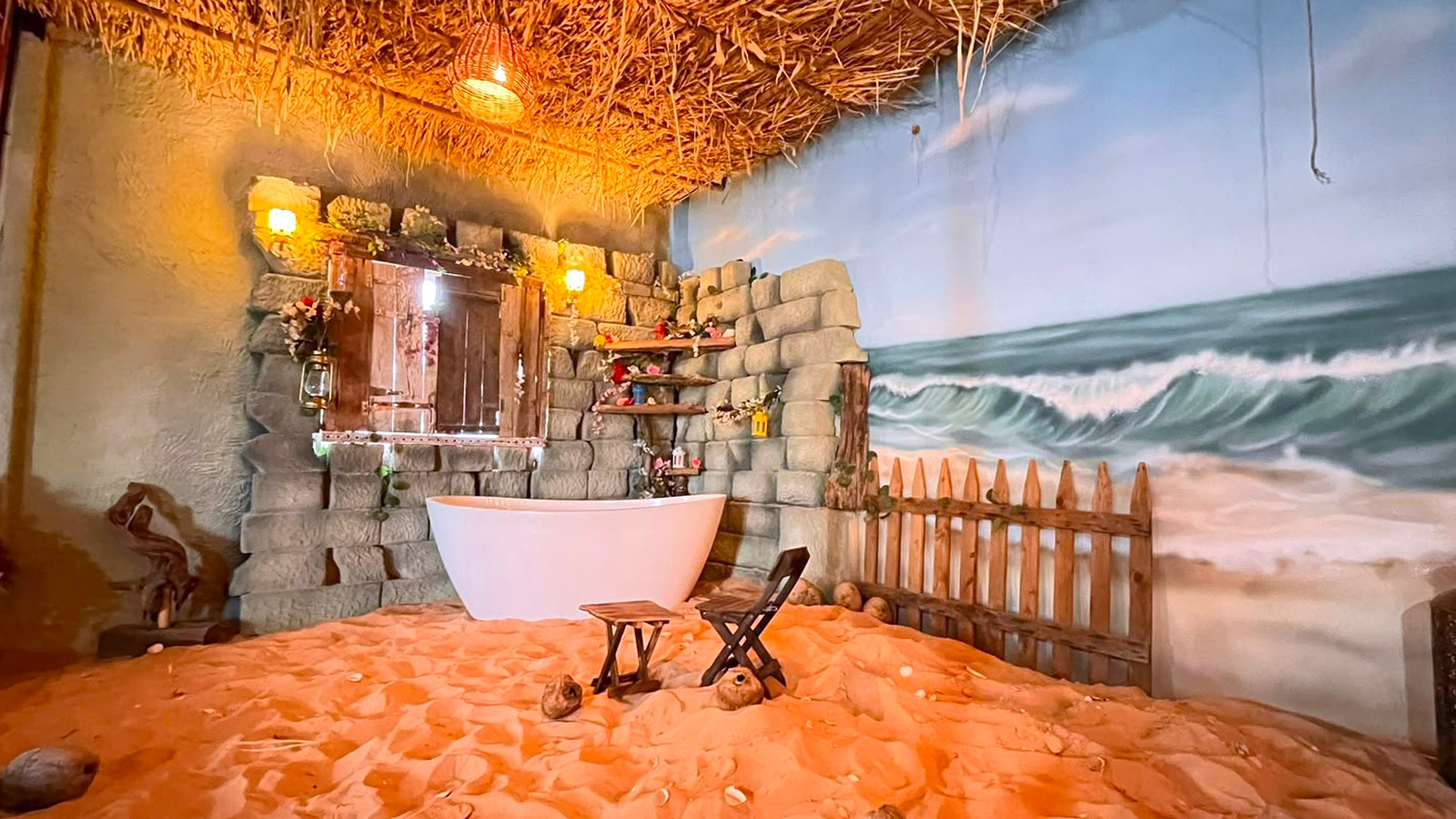 Indoor beach-themed photography set with sand, coconuts, a white tub and a painted ocean mural