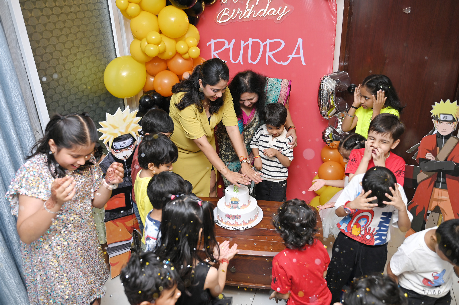 Children surrounding the birthday boy and his family during a lively Naruto-themed cake-cutting moment