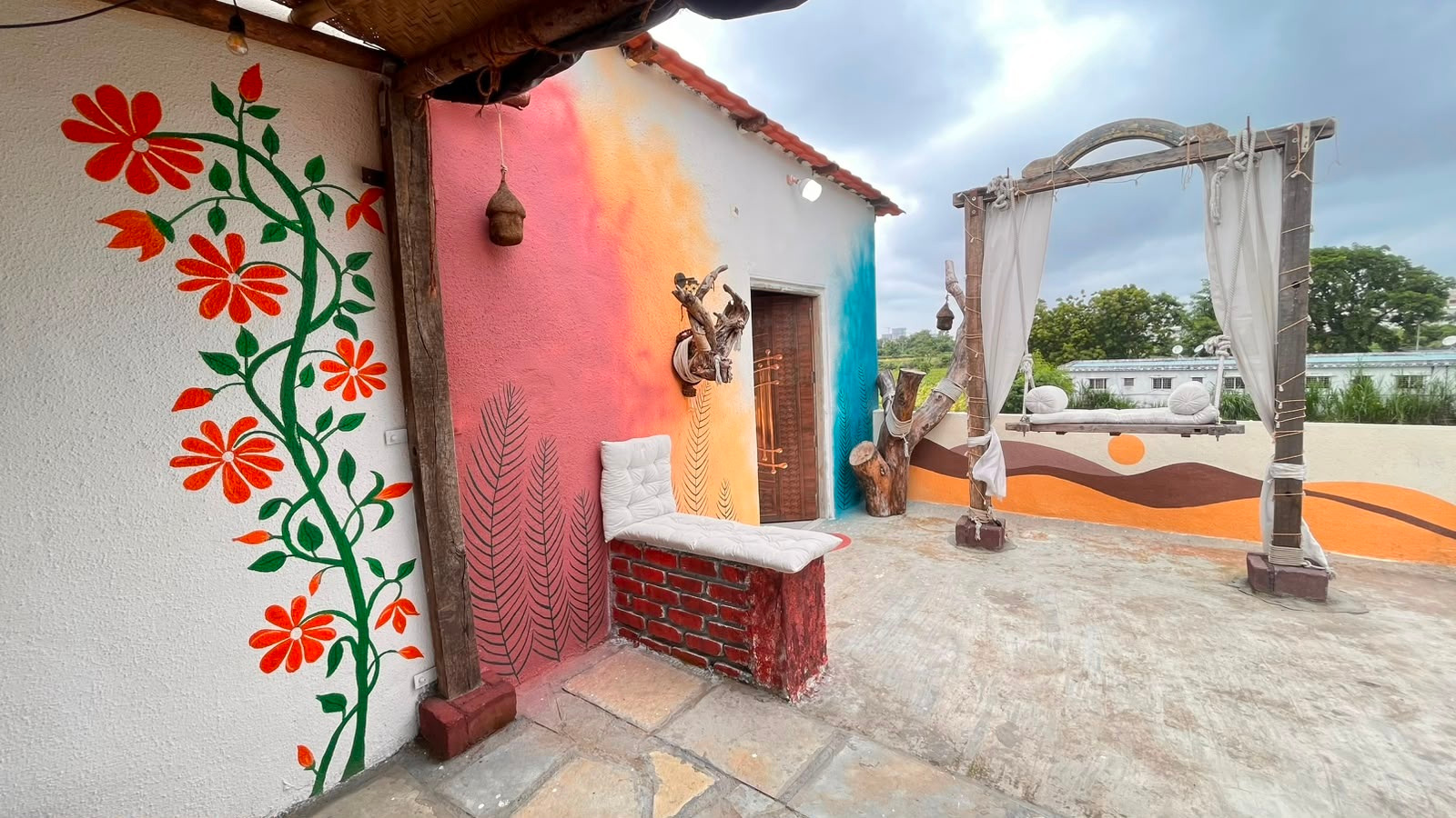 Colourful rooftop studio terrace with floral wall art, white seating and a suspended swing