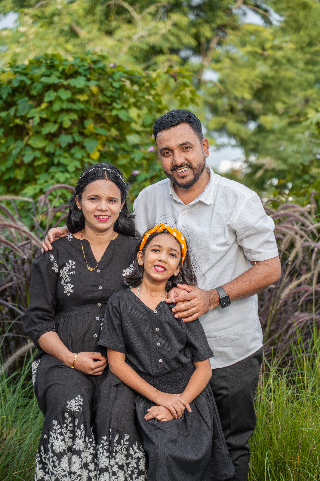 Expectant parents and their daughter posing together in coordinated black-and-white outfits in a garden