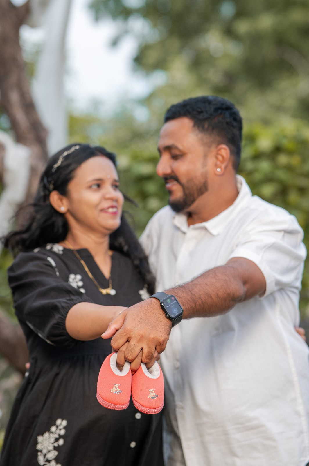 Expectant couple smiling together while holding a pair of small red baby shoes