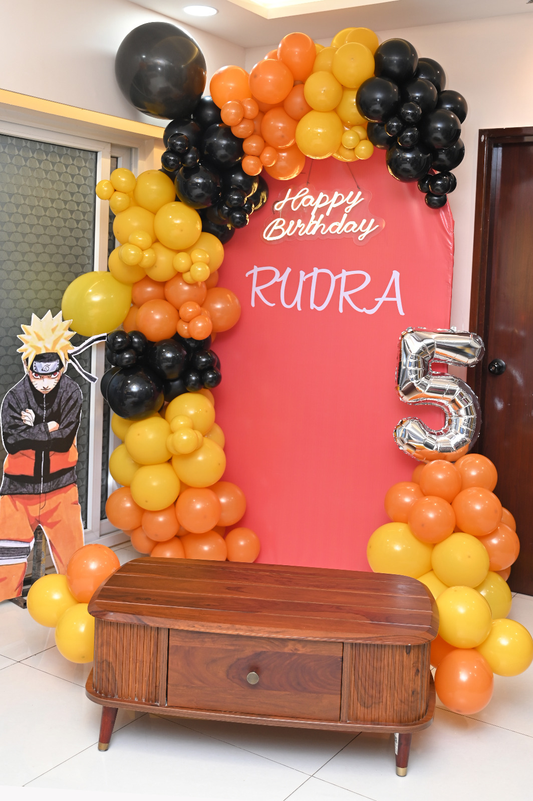 Naruto-themed fifth birthday setup with orange, yellow and black balloons, character cutout and silver number five