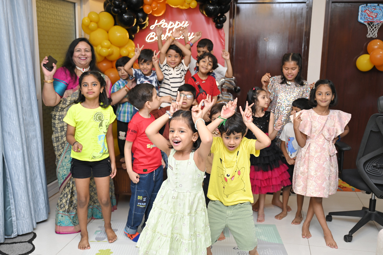 Group of children laughing, dancing and celebrating in front of a colourful birthday balloon backdrop