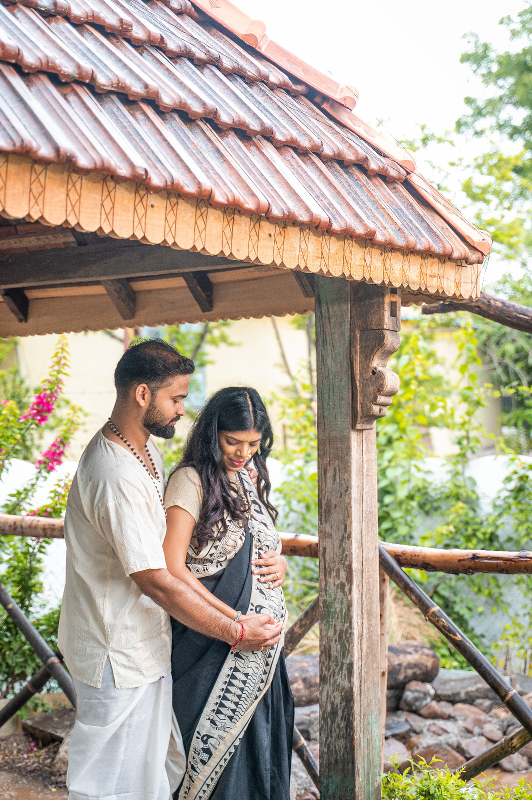 Expectant couple embracing beneath a rustic wooden pavilion in a garden