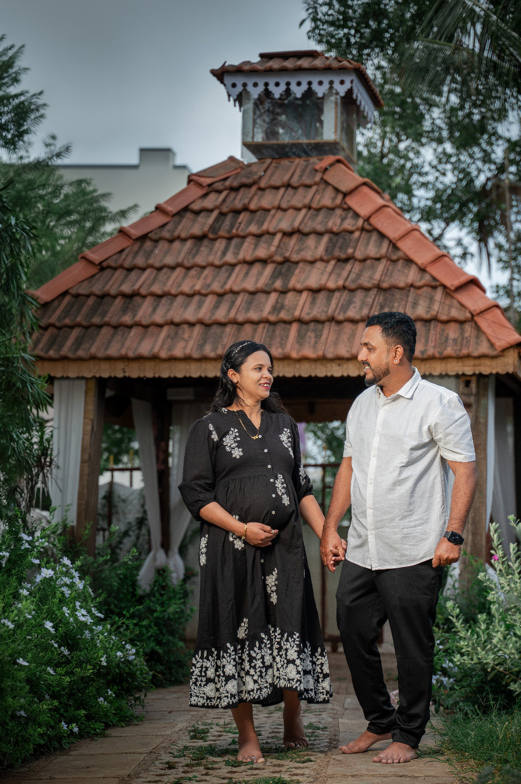 Expectant couple holding hands outside a tiled garden pavilion during a family maternity portrait