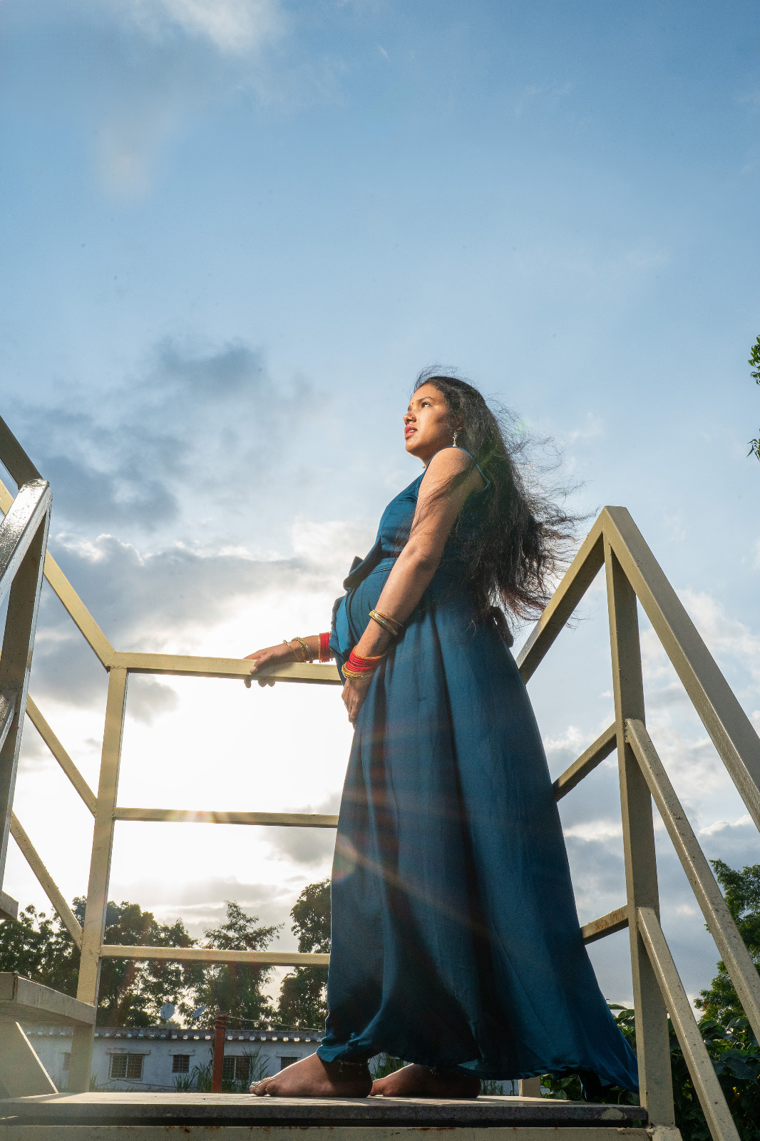 Low-angle maternity portrait of a woman in a blue gown standing against an open sky