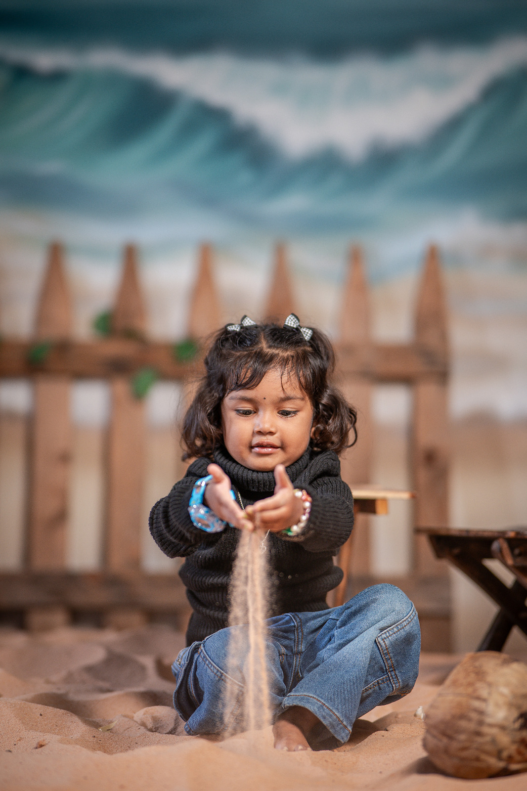 Young girl in a black sweater and blue jeans letting sand fall through her hands in a themed portrait set