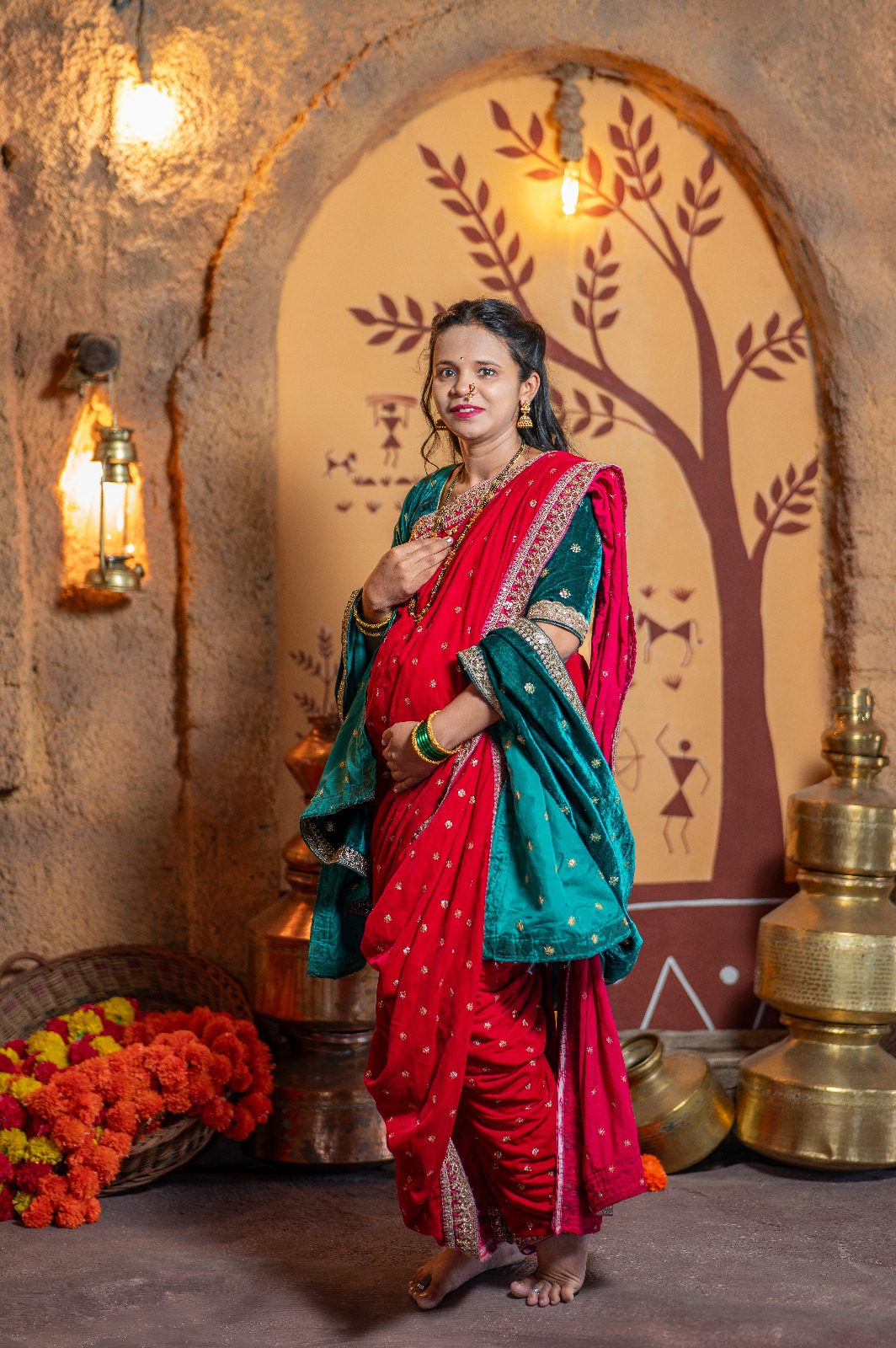 Expectant mother wearing a red traditional saree in a warmly lit heritage studio setting