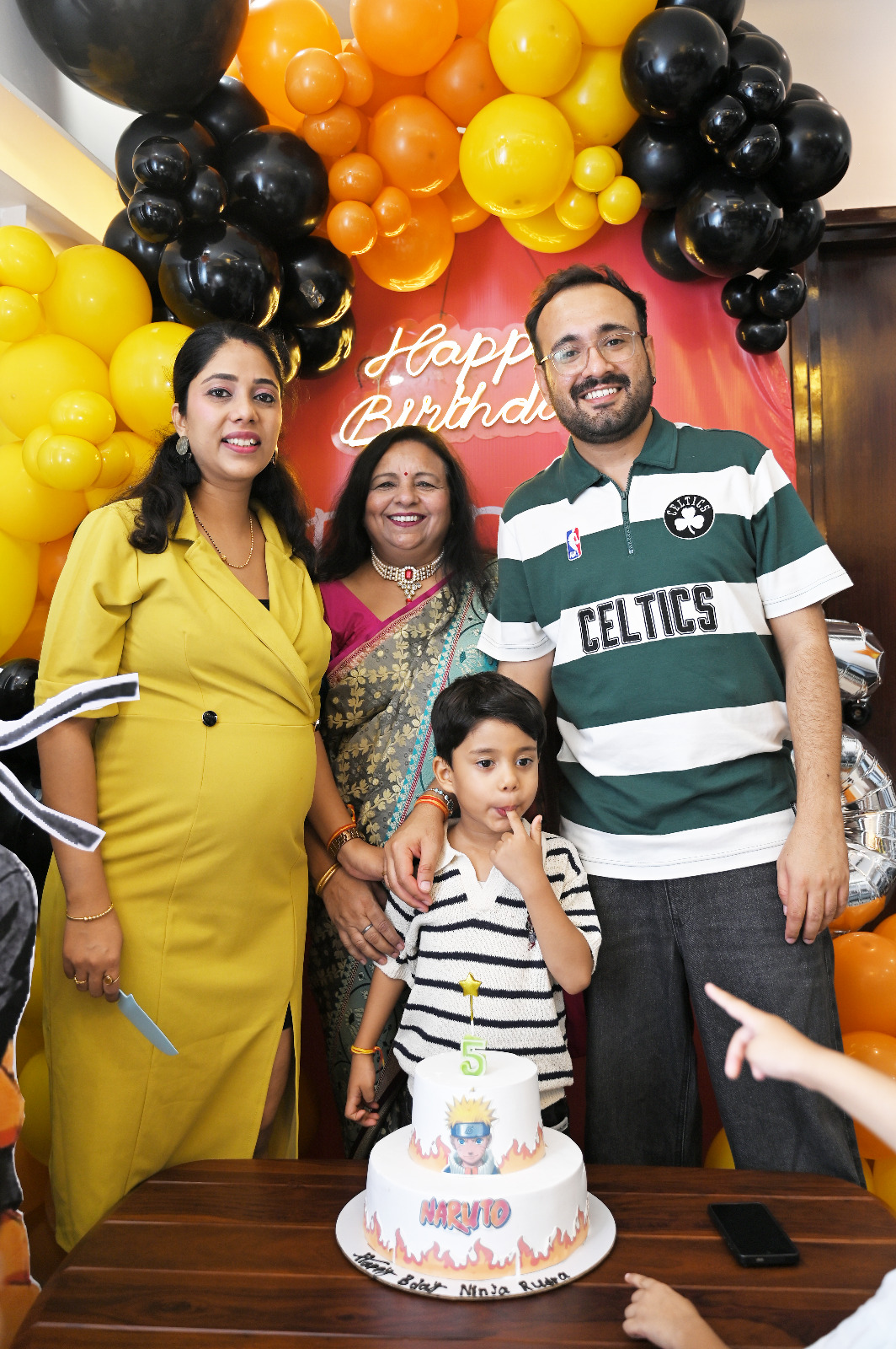 Birthday boy posing with his parents and grandmother behind a Naruto-themed fifth birthday cake