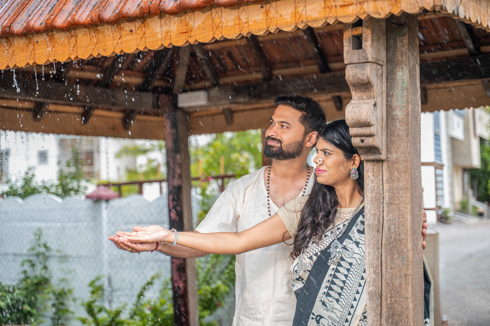 Expectant couple sharing a joyful moment beneath a wooden shelter in the rain